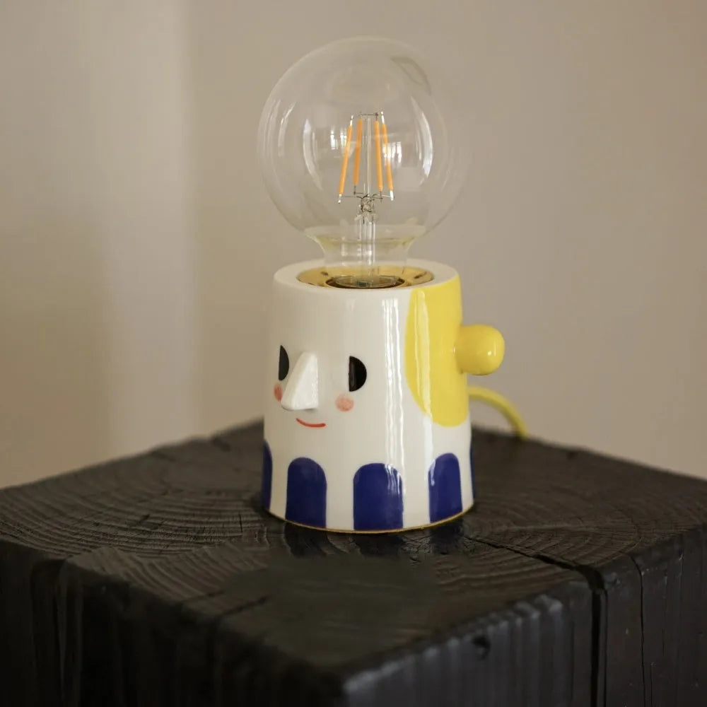Handmade ceramic bedside lamp with a ball headlight design on a nightstand.
