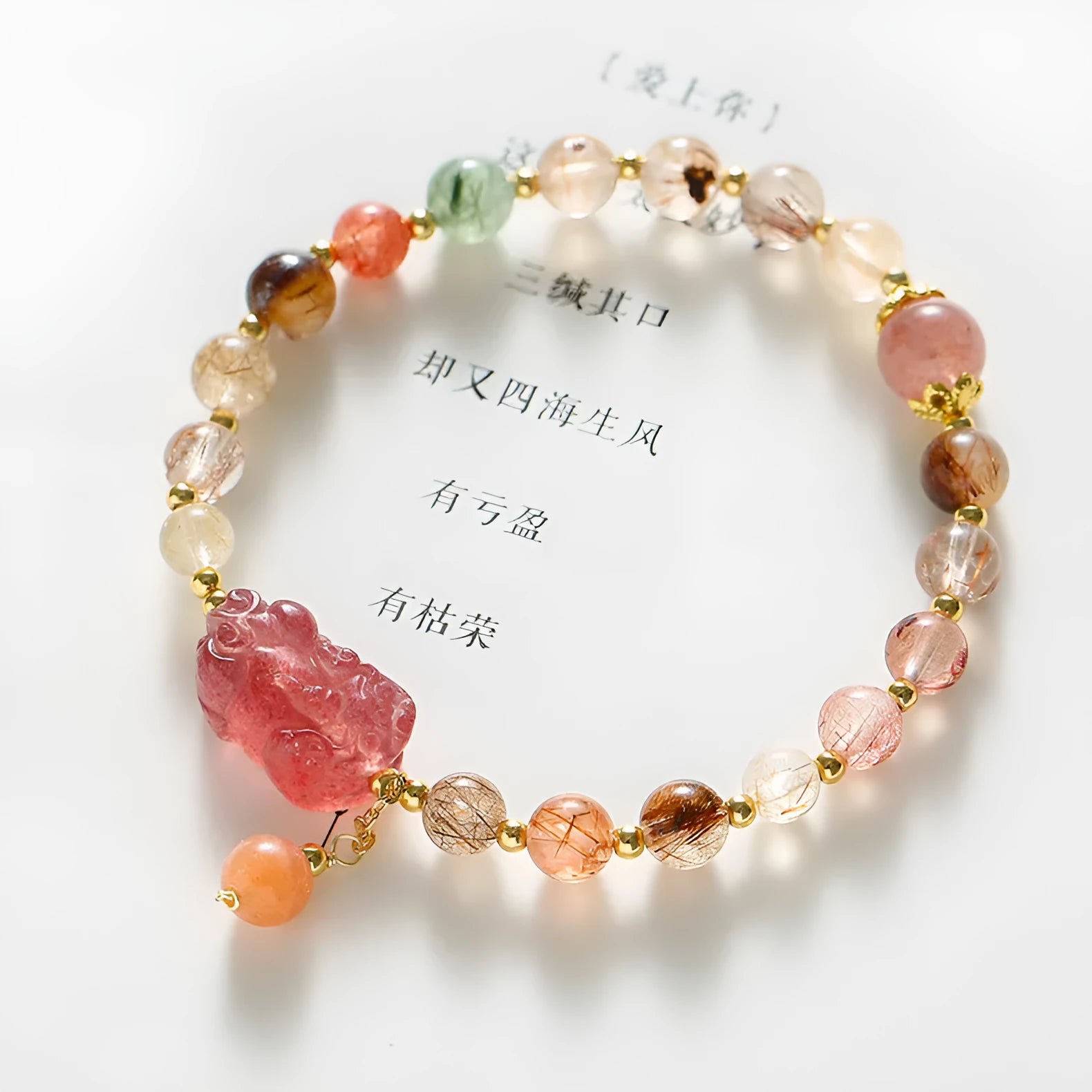 Copper women's bracelet with a pink Strawberry Quartz crystal and a gold-toned Pixiu charm, alongside smaller crystal beads.