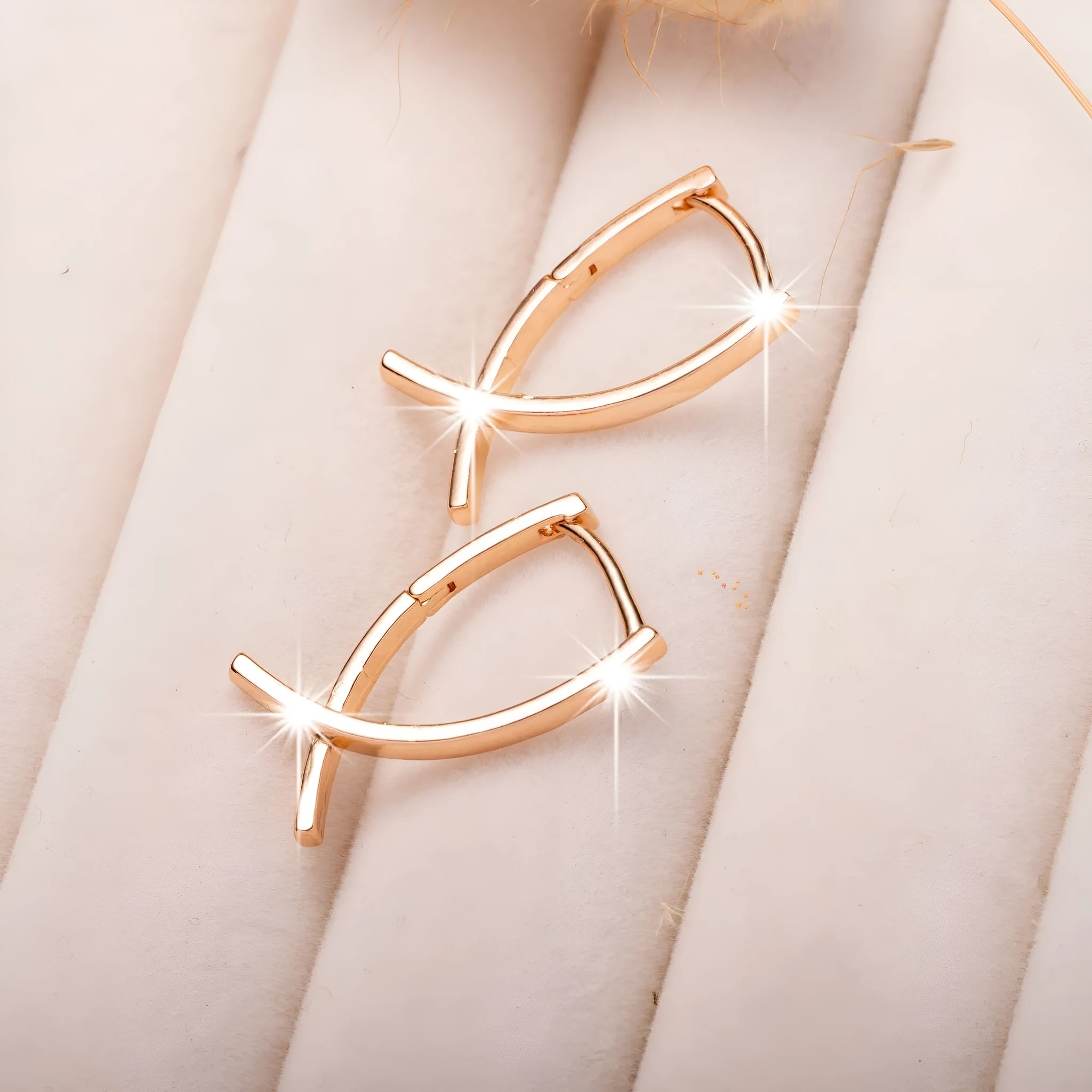 A pair of rose gold coloured cross-shaped earrings made from copper on a plain background.