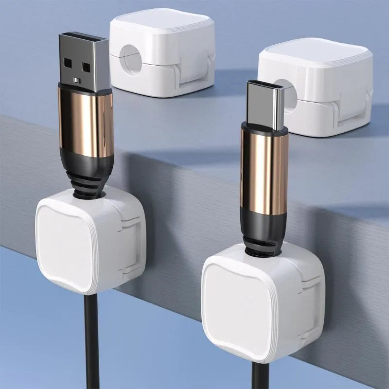 White and black magnetic cable clips with adhesive backing holding a USB cable against a wooden desk edge.