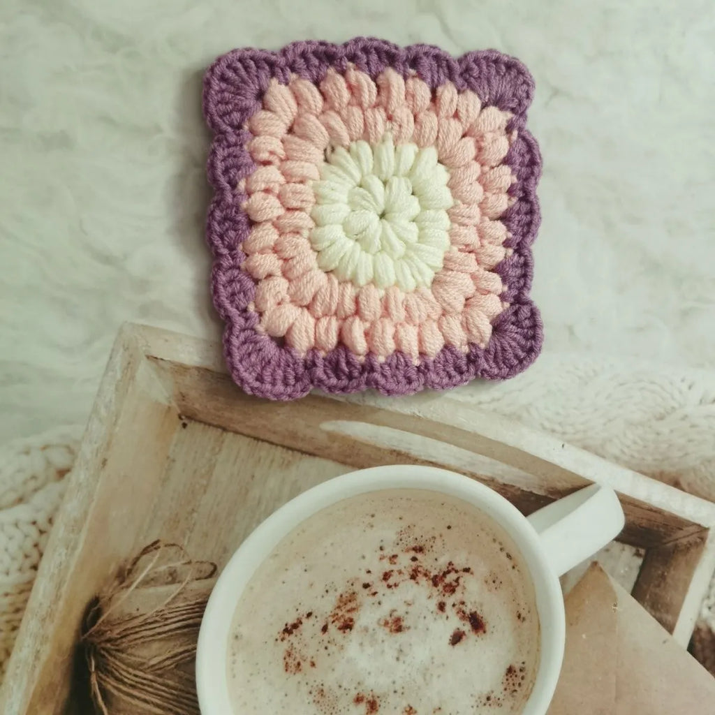Handmade crocheted wool cup placemat with a grandmother lattice design on a wooden table.