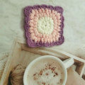 Handmade crocheted wool cup placemat with a grandmother lattice design on a wooden table.