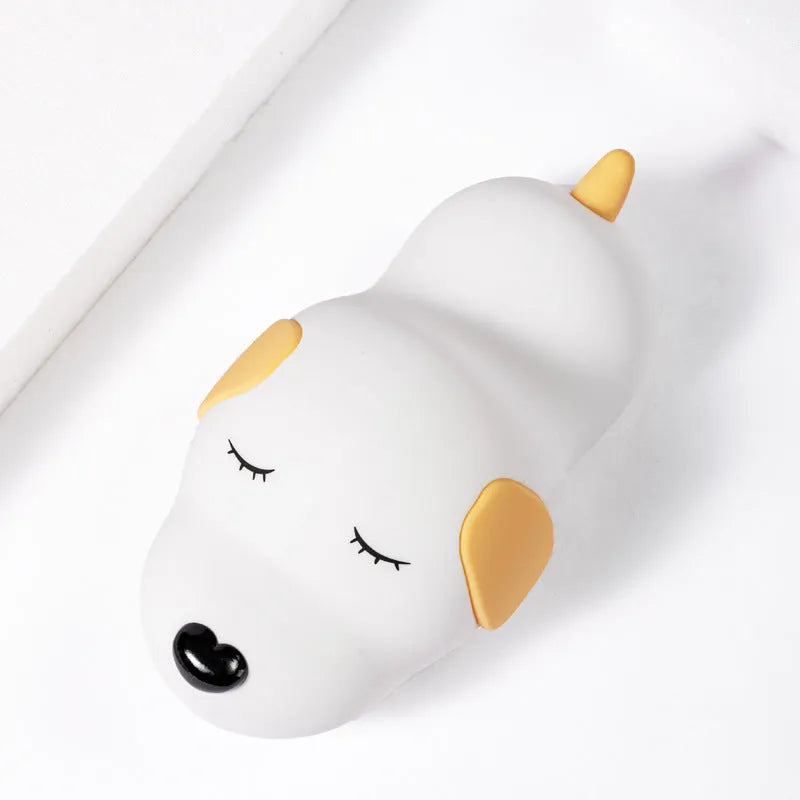 Soft silicone cartoon dog night light with USB cable on a bedside table.
