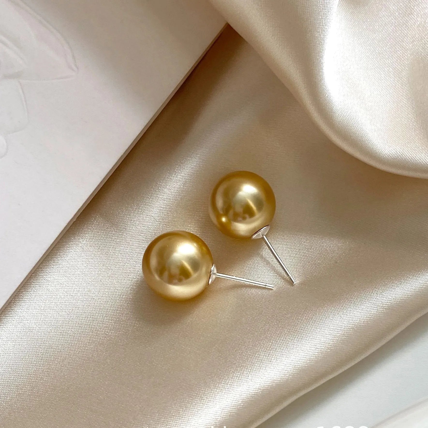 A pair of large geometric silver stud earrings with a central pearl and an eight-point star design detail.