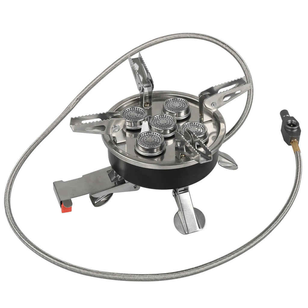 Silver portable split camping stove with foldable legs and a long black hose, on a grass background.