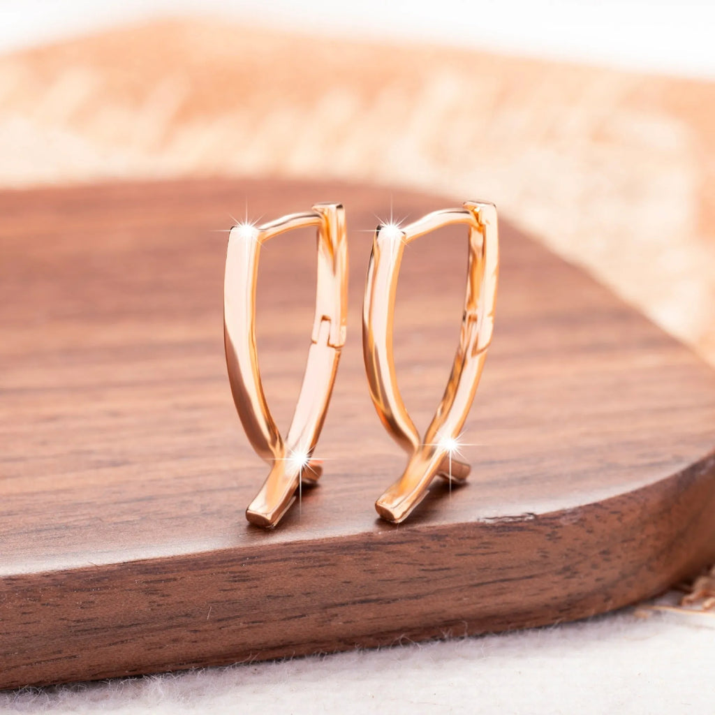 A pair of rose gold coloured cross-shaped earrings made from copper on a plain background.
