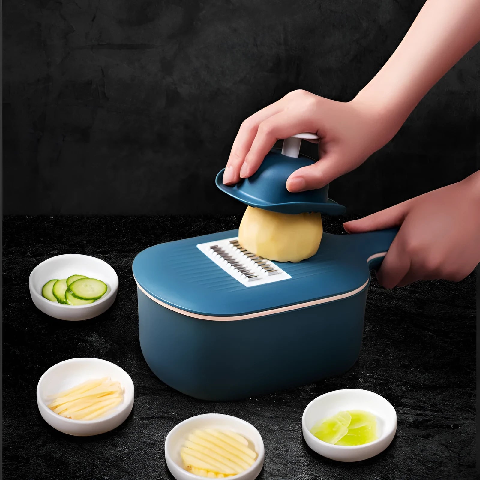 Dark blue vegetable cutter with four stainless steel blades, drain basket, and hand protection guard on kitchen counter