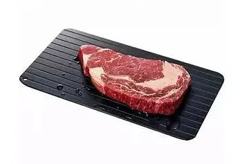 Black aluminium quick defrosting tray for thawing meat and frozen food on a kitchen counter.