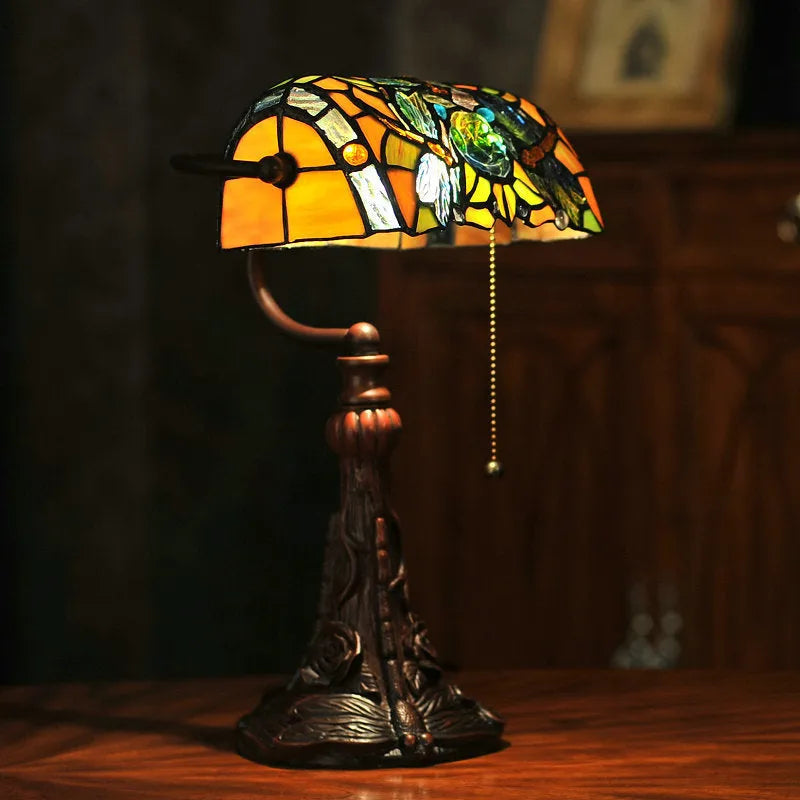 Tiffany style desk lamp with coloured stained glass shade and resin base on a wooden table.