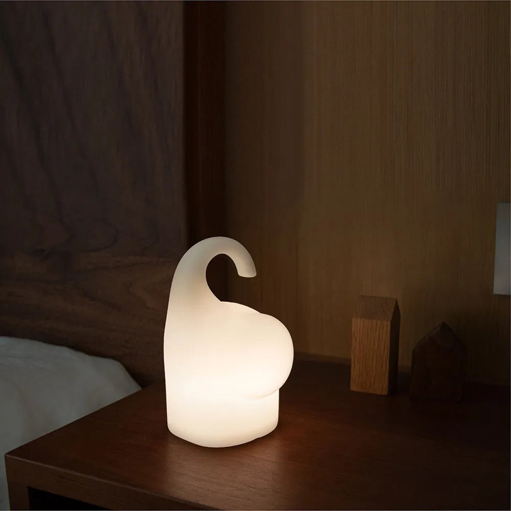 White elephant silicone night light with warm glow on a bedside table.