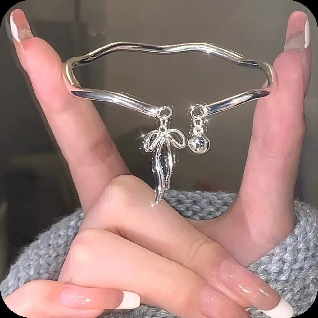 Adjustable silver women's bracelet with a bow bell charm on a white background.