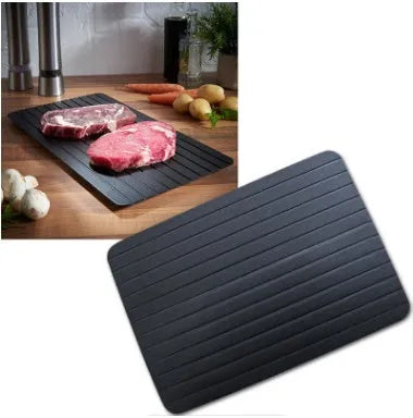 Black aluminium quick defrosting tray for thawing meat and frozen food on a kitchen counter.