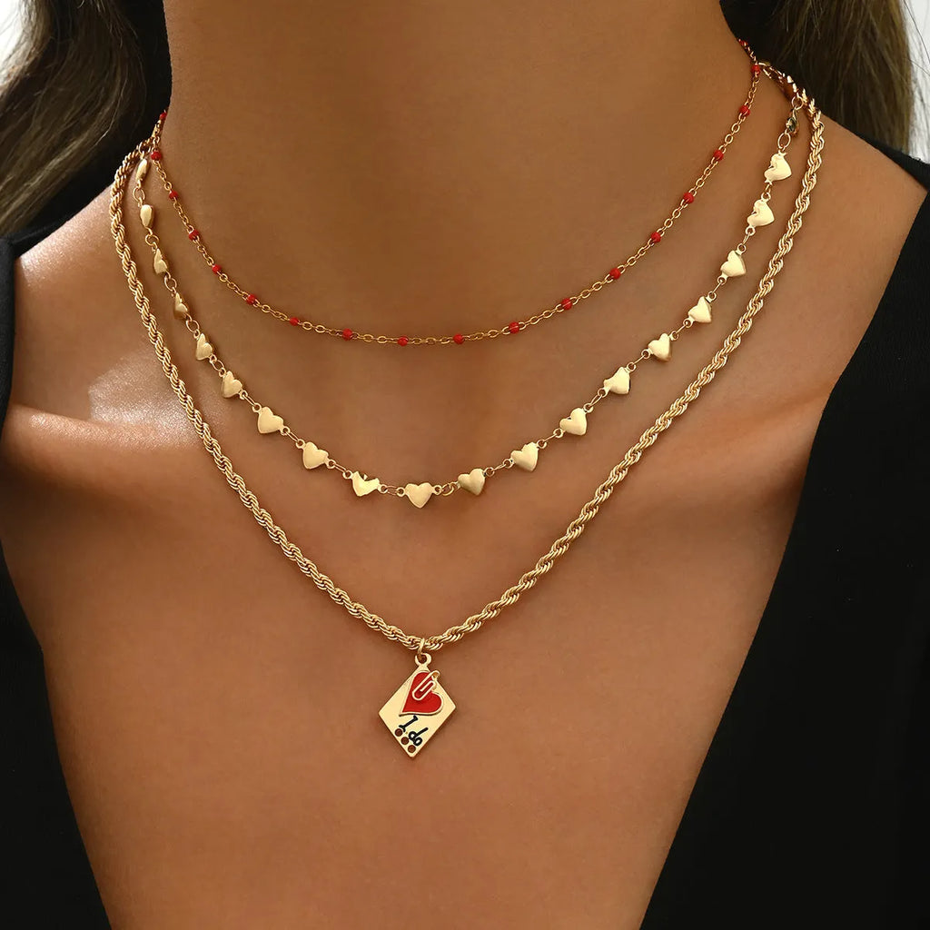 Close-up of a silver-toned three-layer necklace with small geometric heart pendants on an adjustable chain.