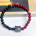 Close-up of handmade obsidian-colour bead bracelet with metal cat charm on adjustable red string.