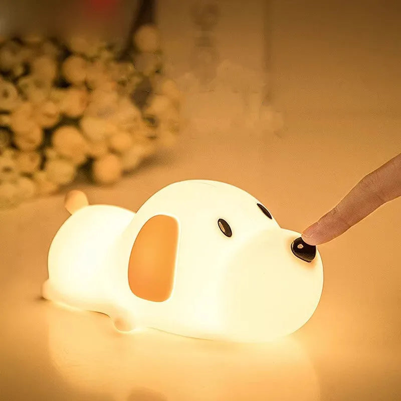Soft silicone cartoon dog night light with USB cable on a bedside table.