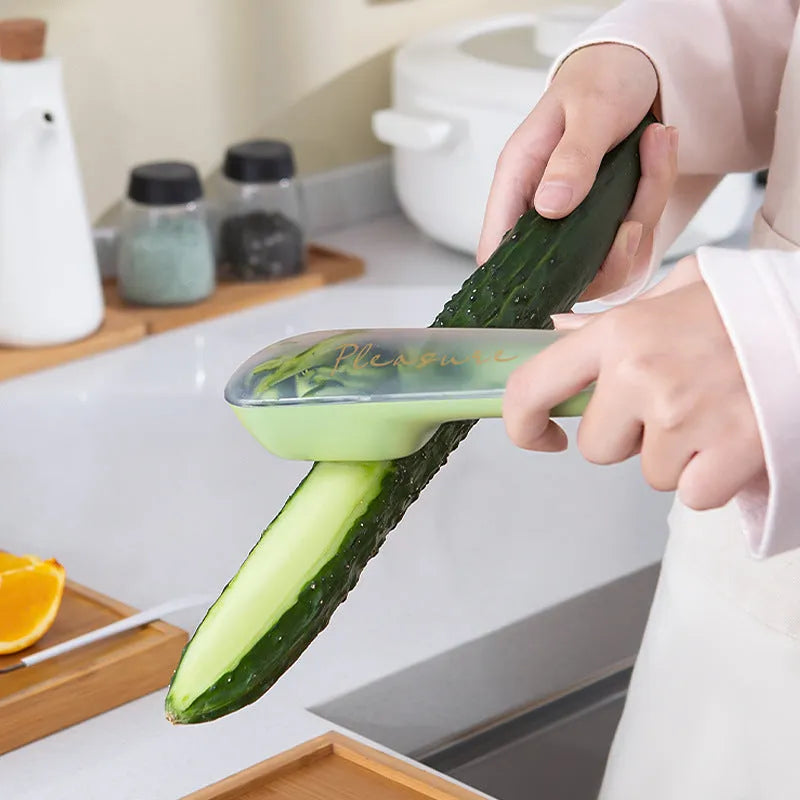 Dark green kitchen peeler with a storage tube, stainless steel blade, and non-slip plastic handle on a worktop.