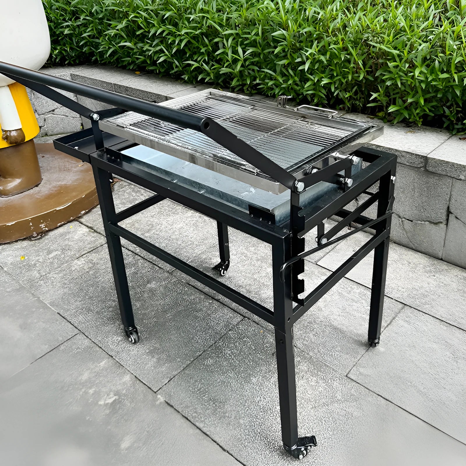 Large portable charcoal barbecue grill with a foldable metal frame set up in a garden.