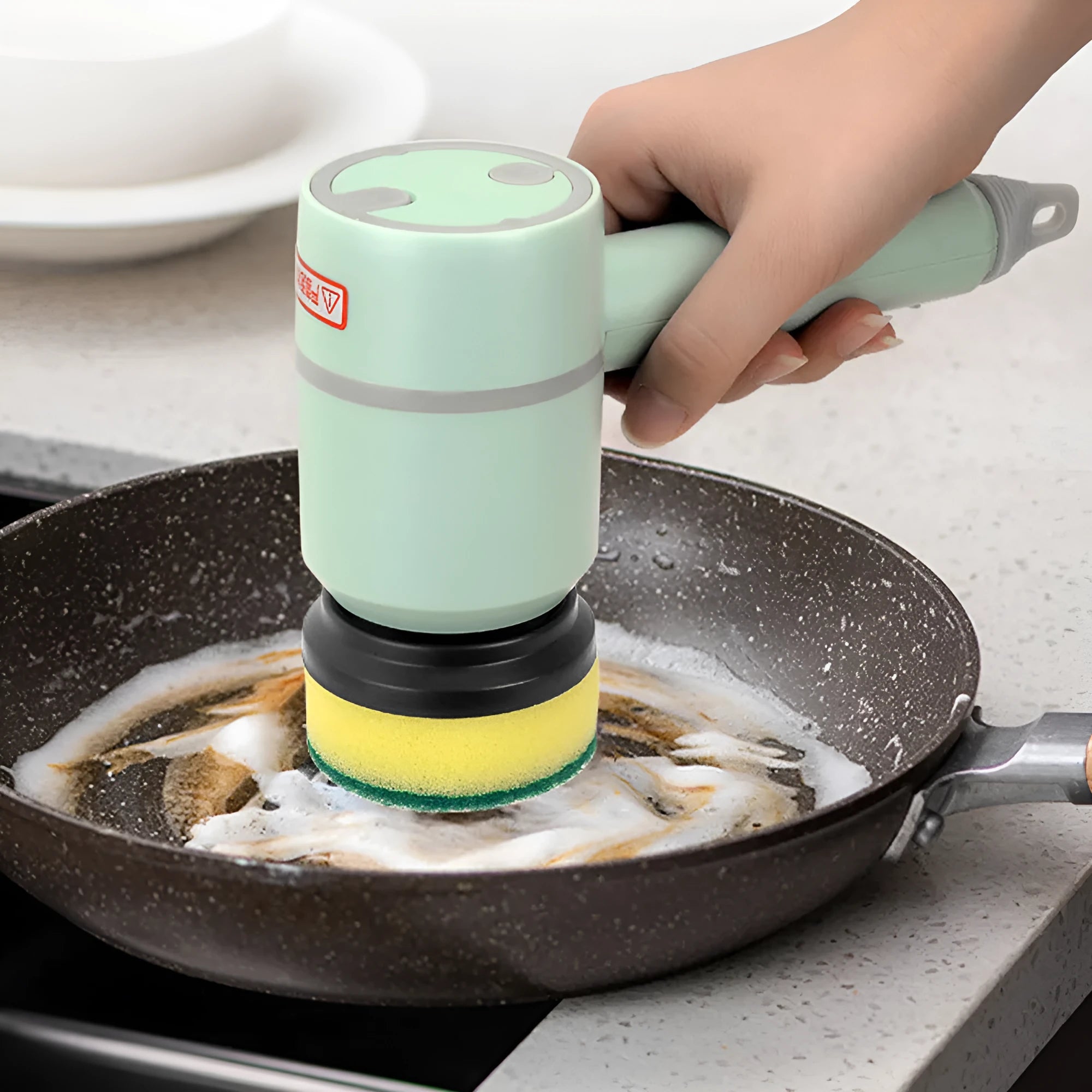 Green electric cleaning brush with multiple rotating brush heads on a kitchen countertop.