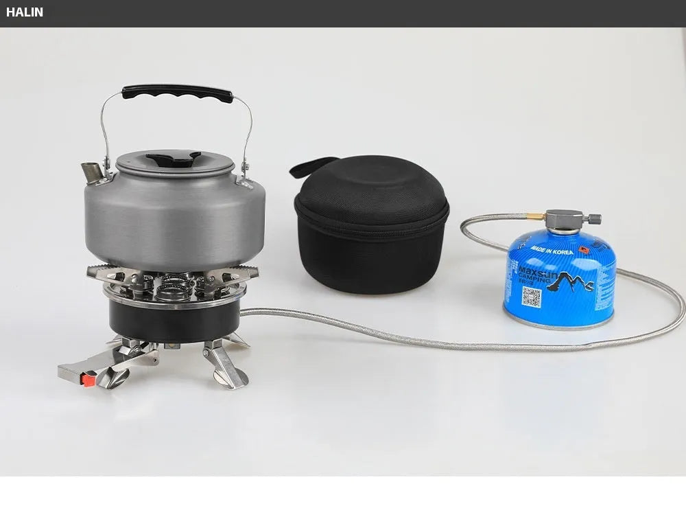 Silver portable split camping stove with foldable legs and a long black hose, on a grass background.