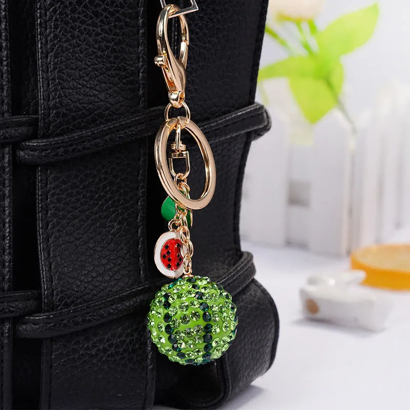 Green watermelon-shaped metal keychain with sparkling crystal details on a white background.