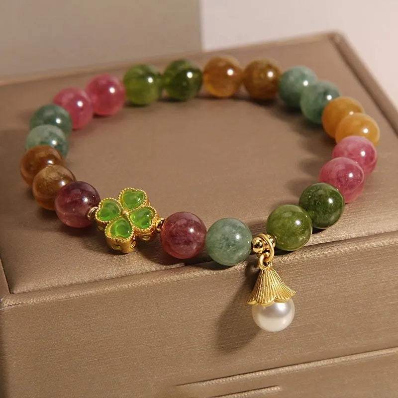 Close-up of a women's silver-toned bracelet with a four-leaf clover charm, pearl pendant, and colourful tourmaline stones.