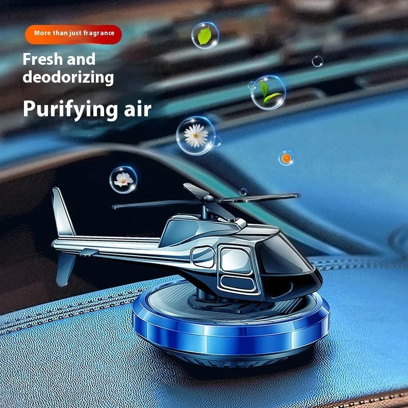 Silver solar-powered metal helicopter car air freshener with rotating blades on a dashboard.