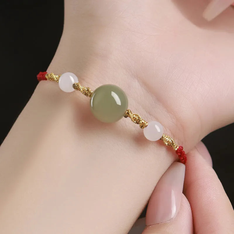 Hand-woven red rope bracelet with Hetian jade lucky charm beads on a model's wrist.