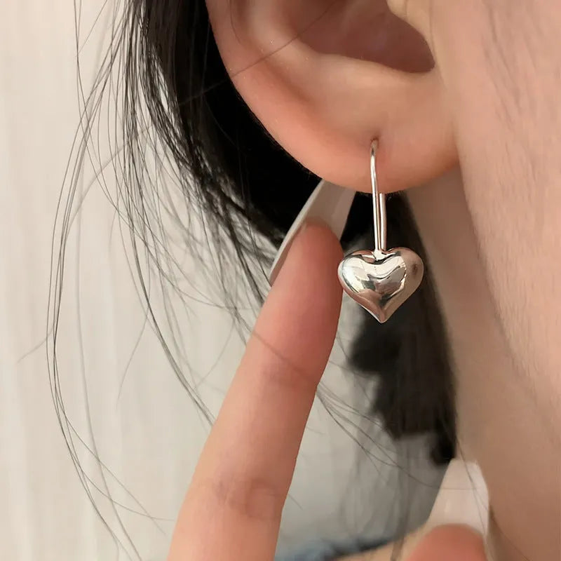 Silver-coloured three-dimensional heart-shaped earrings with glossy finish on copper