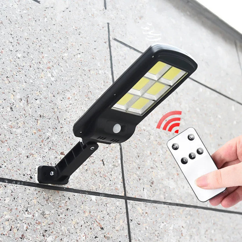 Black outdoor solar-powered security light with motion sensor on a wall.