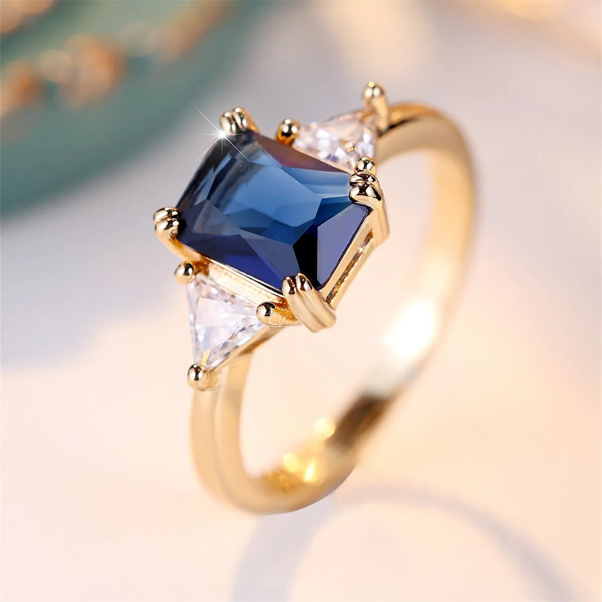 A rectangular gold sapphire blue plated copper ring for women on a plain background.