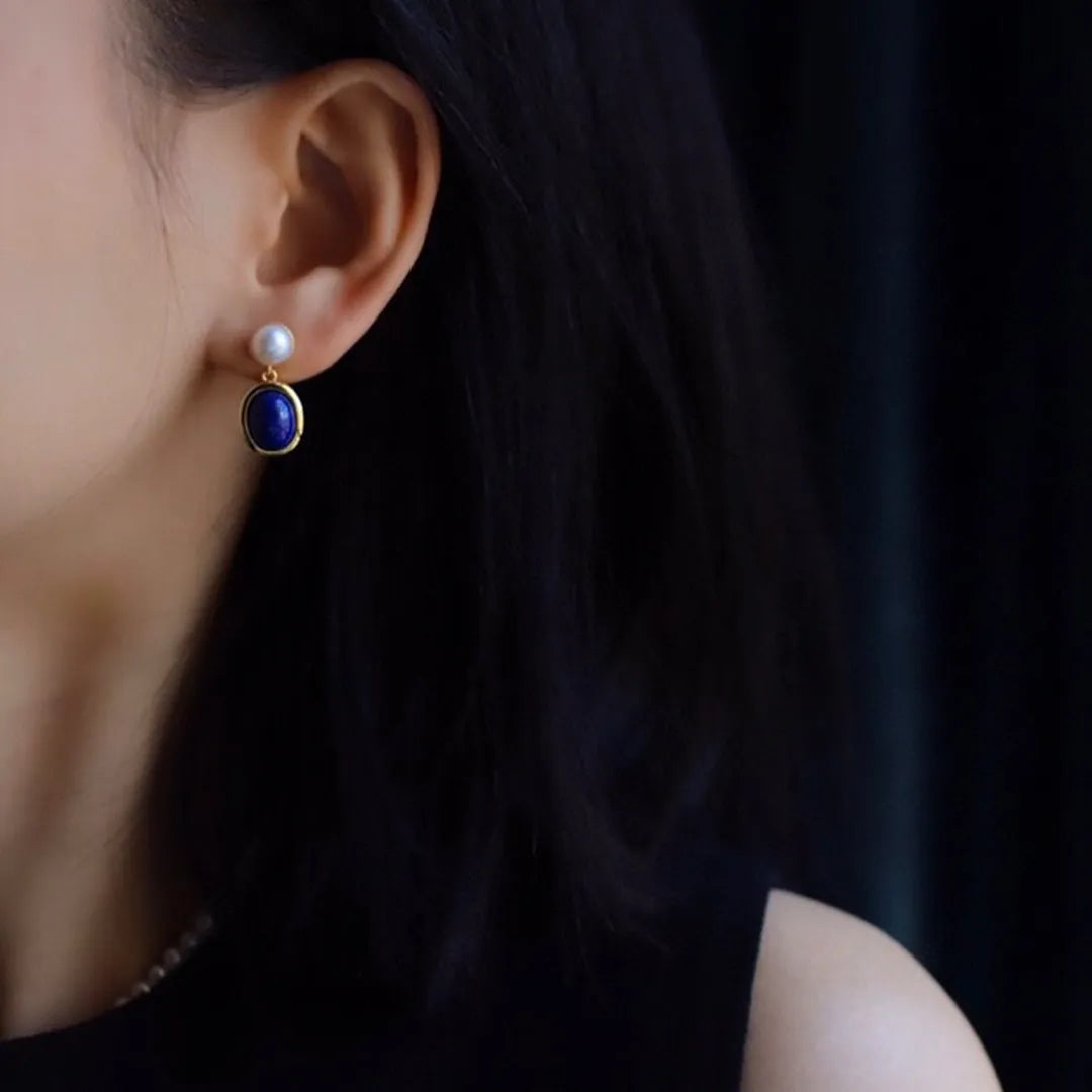 A pair of simple silver earrings with blue lapis lazuli pearls and auspicious pattern details.