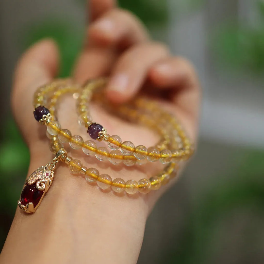 Handmade gold rutilated quartz bracelet with three-circle Chinese design and hanging chopsticks.