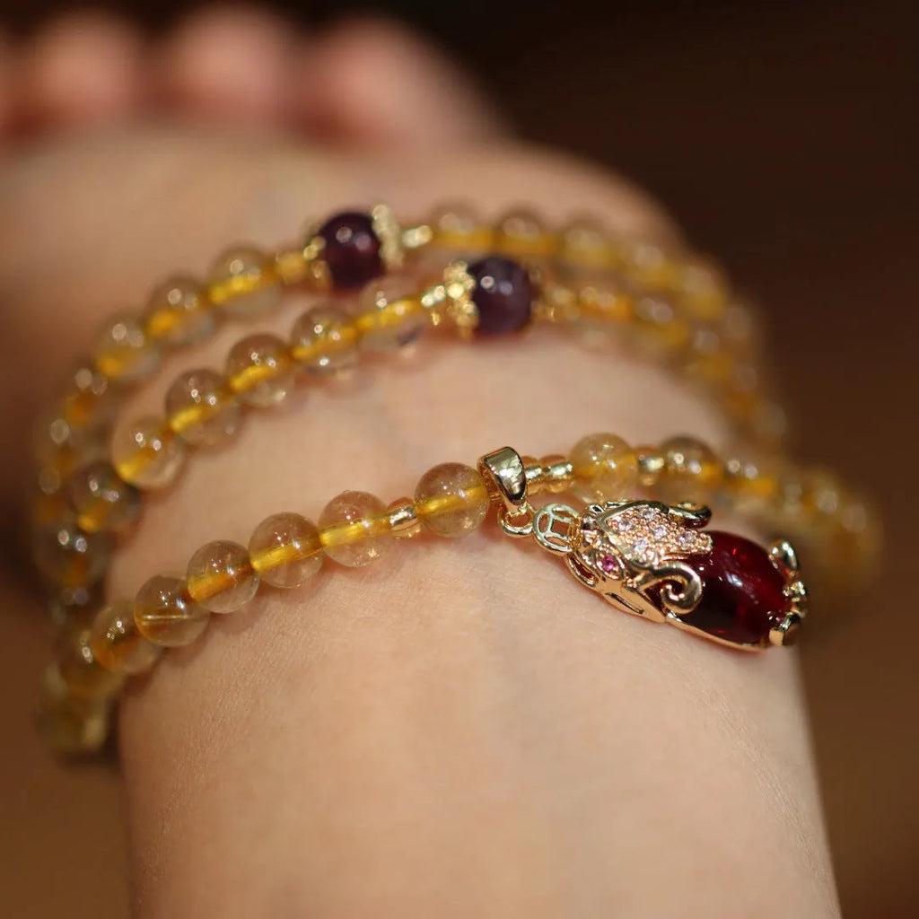 Handmade gold rutilated quartz bracelet with three-circle Chinese design and hanging chopsticks.