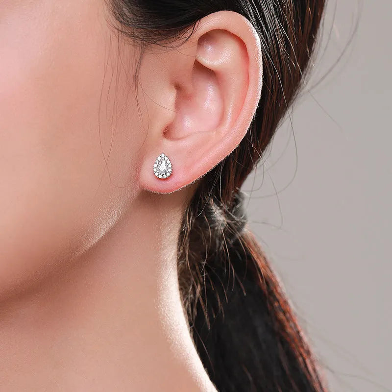 Close-up of a pair of women's silver water drop shaped ear studs on a plain background.