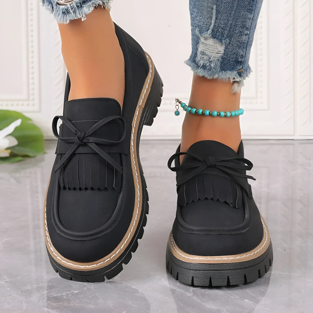 Black women's loafers with a tassel and bow knot on a chunky rubber sole.