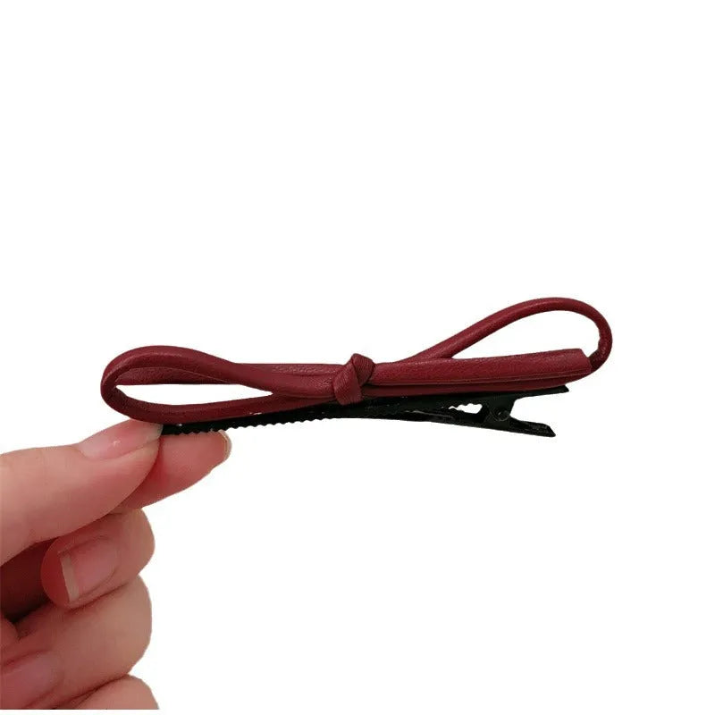 Wine red leather hair clip with a classic bow design on a white background.