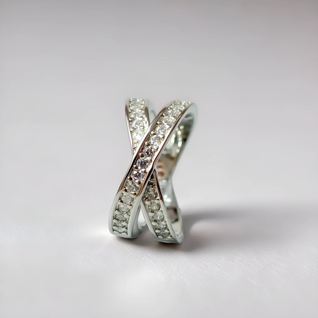 A silver geometric cross ring with micro-inlaid zircon stones on a finger, showing side profile.