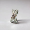 A silver geometric cross ring with micro-inlaid zircon stones on a finger, showing side profile.