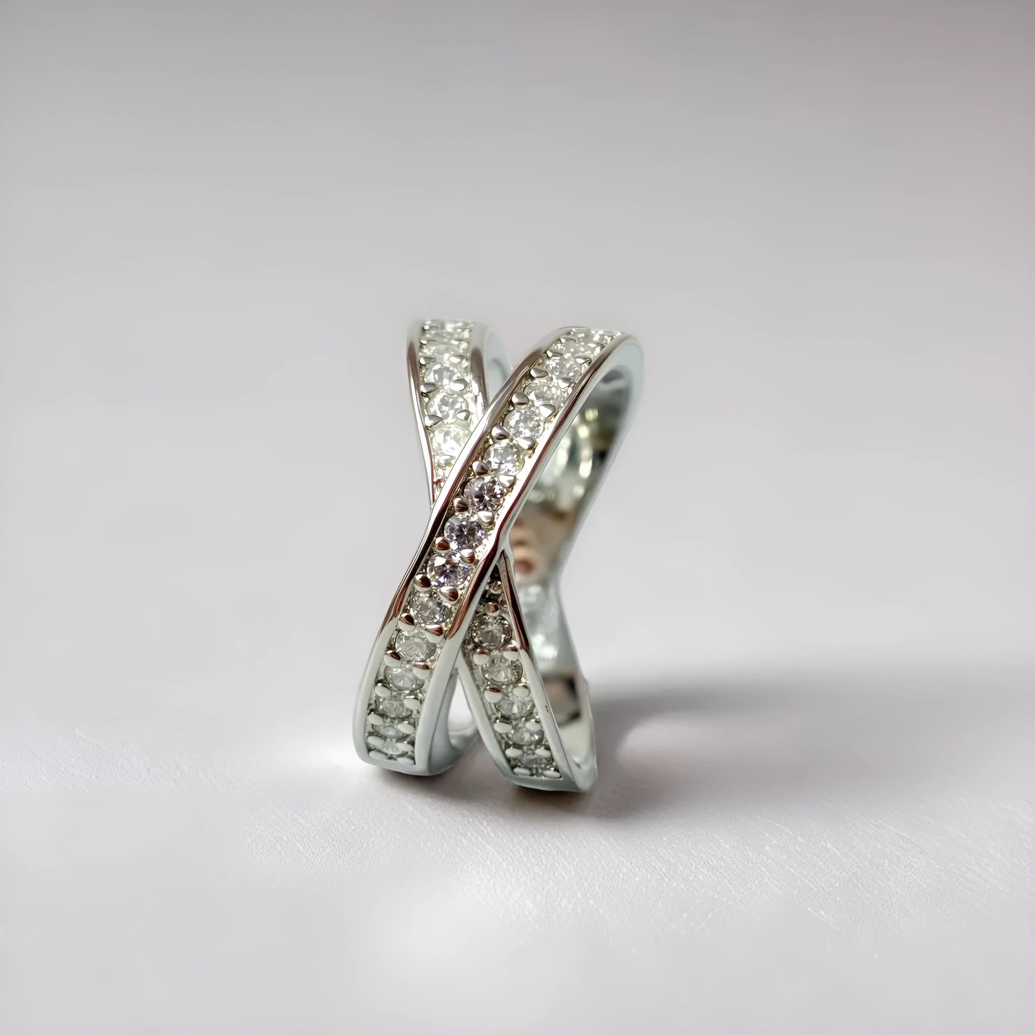 A silver geometric cross ring with micro-inlaid zircon stones on a finger, showing side profile.