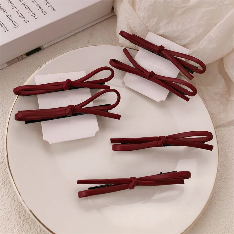 Wine red leather hair clip with a classic bow design on a white background.