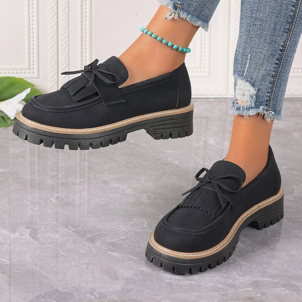 Black women's loafers with a tassel and bow knot on a chunky rubber sole.