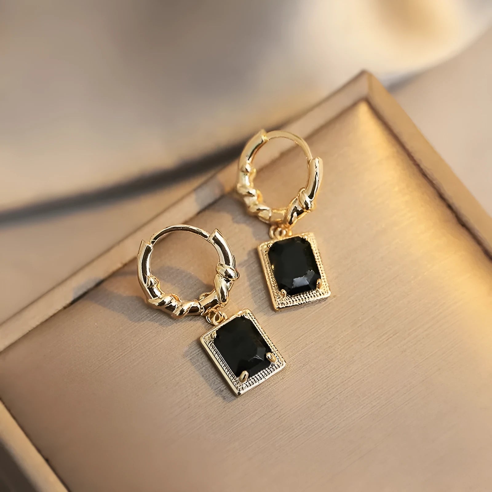 A pair of geometric copper earrings with black zircon stones in a quadrilateral shape.