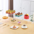 White and transparent plastic cube dessert display stands arranged in a tiered set.