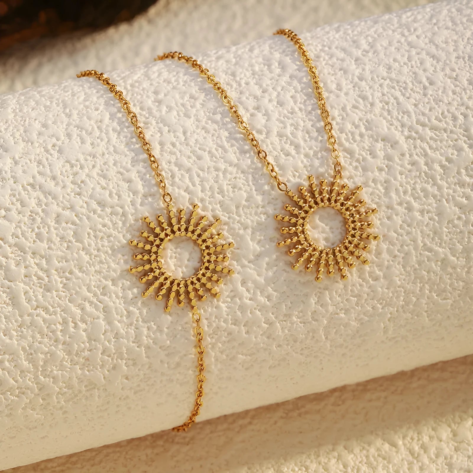 Gold geometric chain necklace and matching bracelet set on a plain background.
