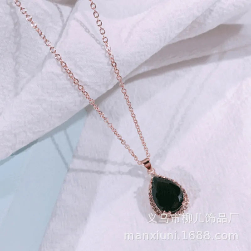Close-up of a women's rose gold tone drop pendant necklace with pink rhinestone inlay on a model.