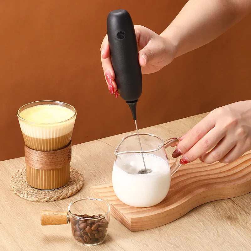 Black and white electric hand-held milk frother for coffee preparation on kitchen counter