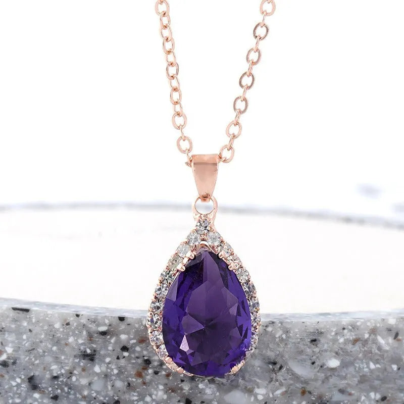 Close-up of a women's rose gold tone drop pendant necklace with pink rhinestone inlay on a model.