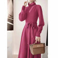 A woman wearing a rose red turtleneck long sleeve knitted dress with an elastic waist and a loose mid-length skirt.