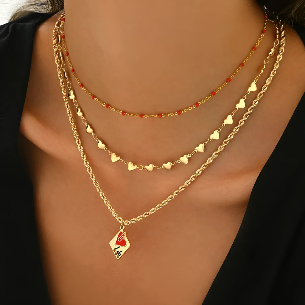 Close-up of a silver-toned three-layer necklace with small geometric heart pendants on an adjustable chain.
