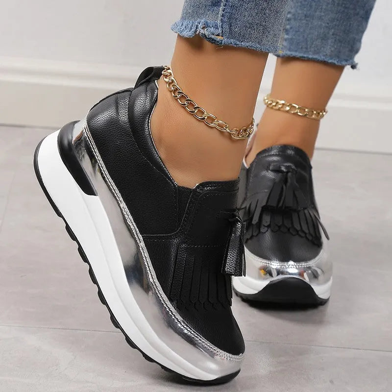 Women's black casual platform shoes with tassel detail and a low wedge heel on a white background.
